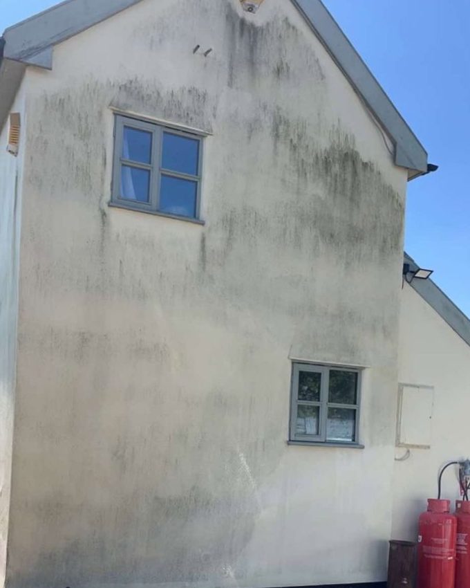 Cream rendered gable wall streaked with green and black algae before cleaning